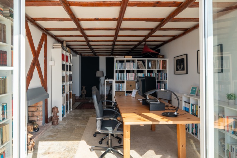 Estúdio de tecto de madeira com biblioteca e mesa comprida