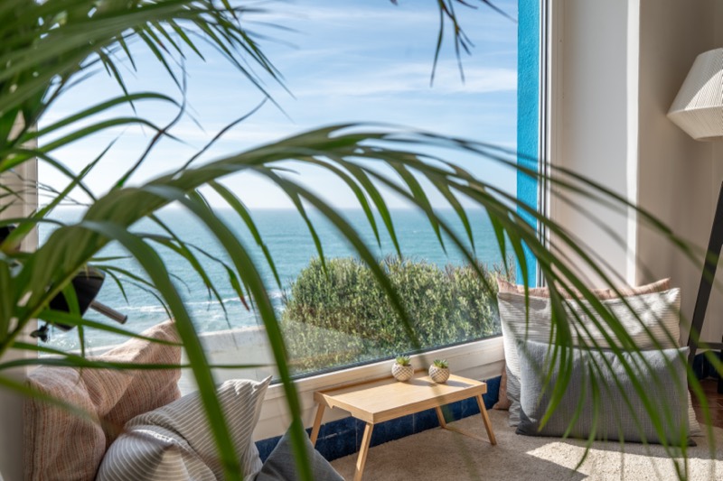 Reading corner by a picture window over the ocean, palm leaves in the foreground